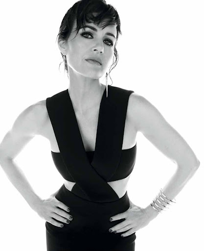 Portrait of a woman with short dark hair wearing a black dress and silver jewelry against a white background