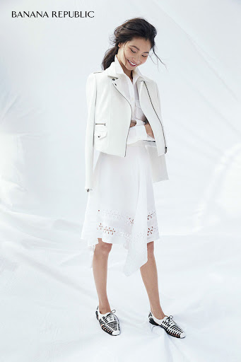 Asian woman in white jacket and eyelet dress posing in bright studio light. Banana Republic logo in upper left corner.