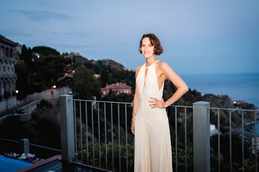 Phoebe Waller-Bridge wearing a cream halter neck gown standing on a balcony at dusk with coastal views