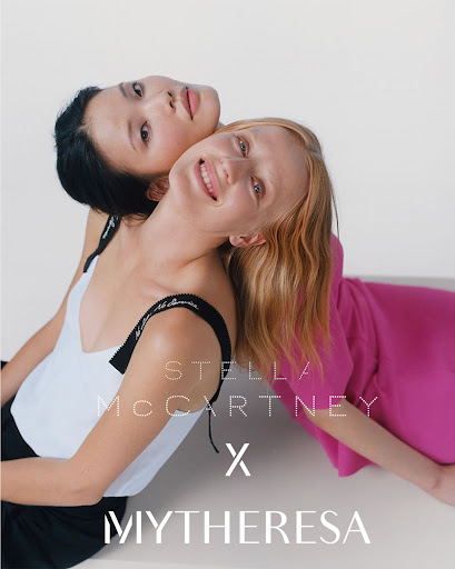 Fashion shot of two women in colorful tops leaning against each other in a photo studio, modeling Stella McCartney x Mytheresa clothing line.