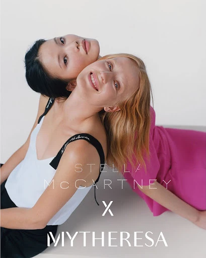 Fashion shot of two women in colorful tops leaning against each other in a photo studio, modeling Stella McCartney x Mytheresa clothing line.