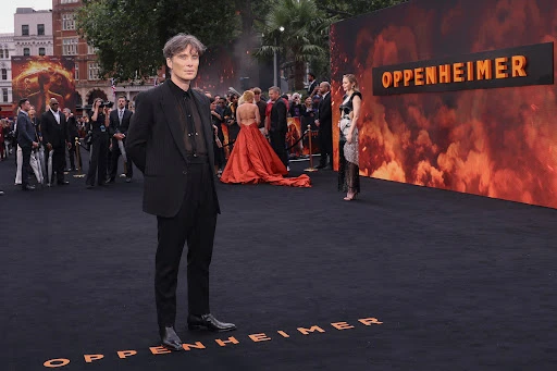Mads Mikkelsen at a red carpet event for the film Oppenheimer, wearing a black suit, surrounded by other celebrities and photographers.