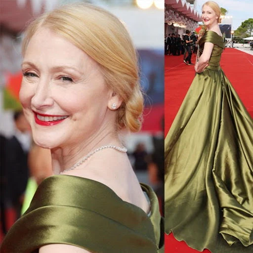 Adult woman in olive gown on red carpet with crowd in background, elegant hairstyle, red lipstick, and jewelry at event.