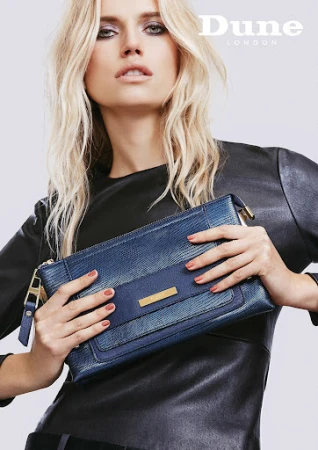 Fashion shot of a blonde model holding a blue Dune London handbag against a neutral background, emphasizing the bag's style and texture.