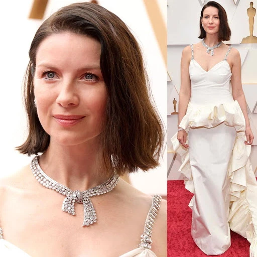 Caitriona Balfe poses in a white dress and diamond necklace on the red carpet at the Oscars. Full and close-up views included.