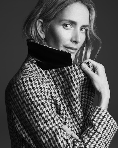 Black and white portrait of a woman wearing a houndstooth coat with a dark collar, looking back over her shoulder.