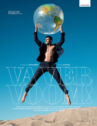 Fashion editorial image featuring a topless man in a suit, holding a globe against a clear blue sky and sandy dunes.