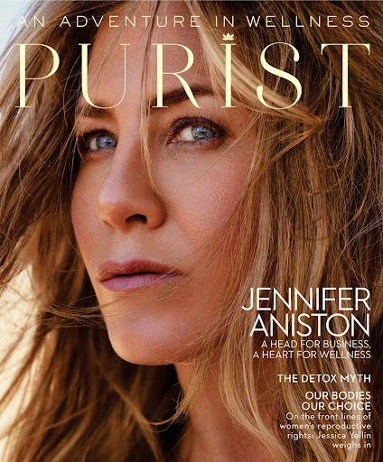 Close-up of Jennifer Aniston on a magazine cover, with blonde hair and blue eyes. The magazine is titled 'Purist' in gold letters.