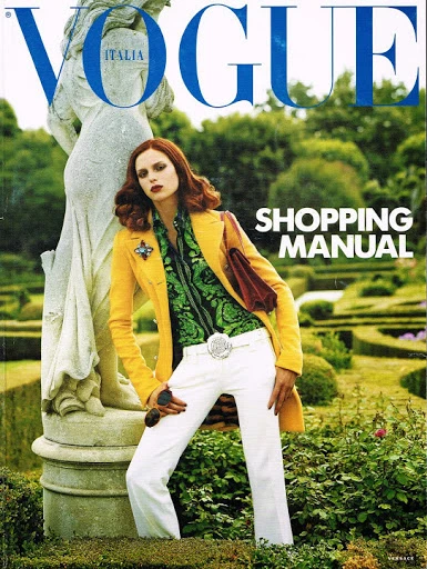 Vogue Italia cover featuring a fashion model in a yellow coat and white pants leaning against a stone statue in a garden setting.