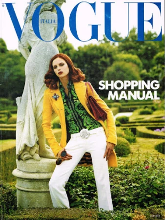 Vogue Italia cover featuring a fashion model in a yellow coat and white pants leaning against a stone statue in a garden setting.