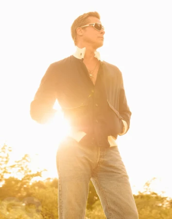 Man wearing sunglasses and jacket outdoors against a bright sky with warm golden backlighting