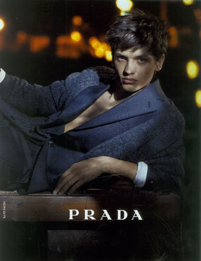 Young male model wearing a dark blue suit jacket outdoors at night with blurred city lights in the background