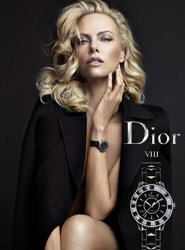 Elegant blonde woman in a black jacket wearing a wristwatch in a fashion advertisement for Dior, set against a dark gray studio backdrop.