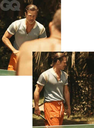 Portrait of adult male, wearing pale blue shirt and orange shorts, holding ping pong paddle, outdoor setting, trees in the background