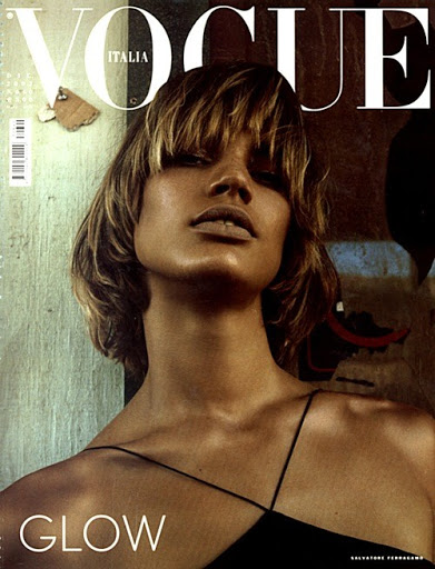 Vogue Italia cover featuring a woman with short blonde hair, dark spaghetti strap top, and glowing skin against a textured background.