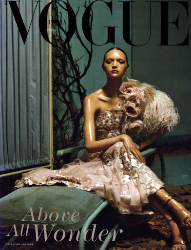 Fashion magazine cover featuring a woman in an ornate, vintage-style dress, posing on a chair against a textured, dark backdrop. Vogue Italia.