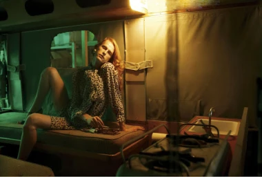 Redheaded woman in a patterned blouse posing on a banquette inside a retro van, color graded by Johnathan Gale
