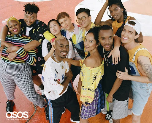 Group of nine diverse young adult models posing together in brightly colored and patterned clothing, smiling, on a painted surface.