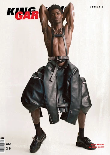 Magazine cover featuring a Black male model wearing a harness and leather jacket, standing against a clean white backdrop in a studio setting.