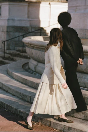 Two models walk on stone steps. One is an African American woman wearing all black. The other is a Caucasian woman wearing a skirt suit.