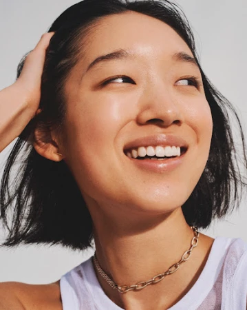 Close-up portrait of an East Asian woman with dark bobbed hair smiling against a plain white background