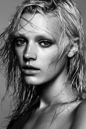 Close-up monochrome portrait of a woman with wet hair and freckles against a neutral background.