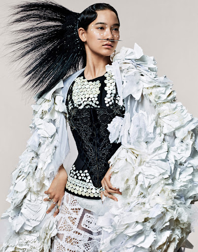 Avant-garde fashion portrait of a woman wearing a black corset and oversized white textured coat against a neutral backdrop in a photo studio.