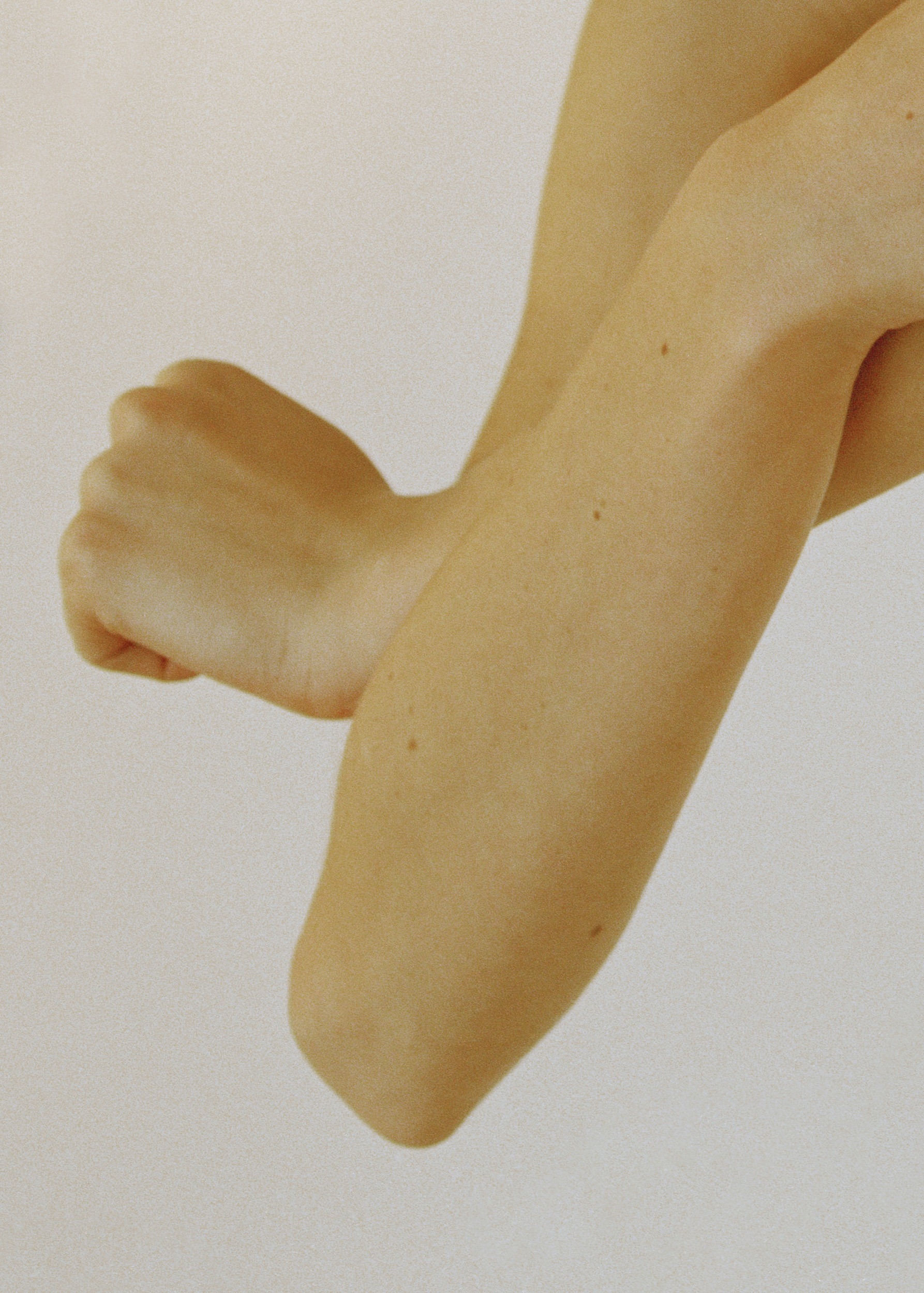 Close-up shot featuring crossed arms and fists of an adult woman, showcasing skin texture and minimalist composition against a white background.