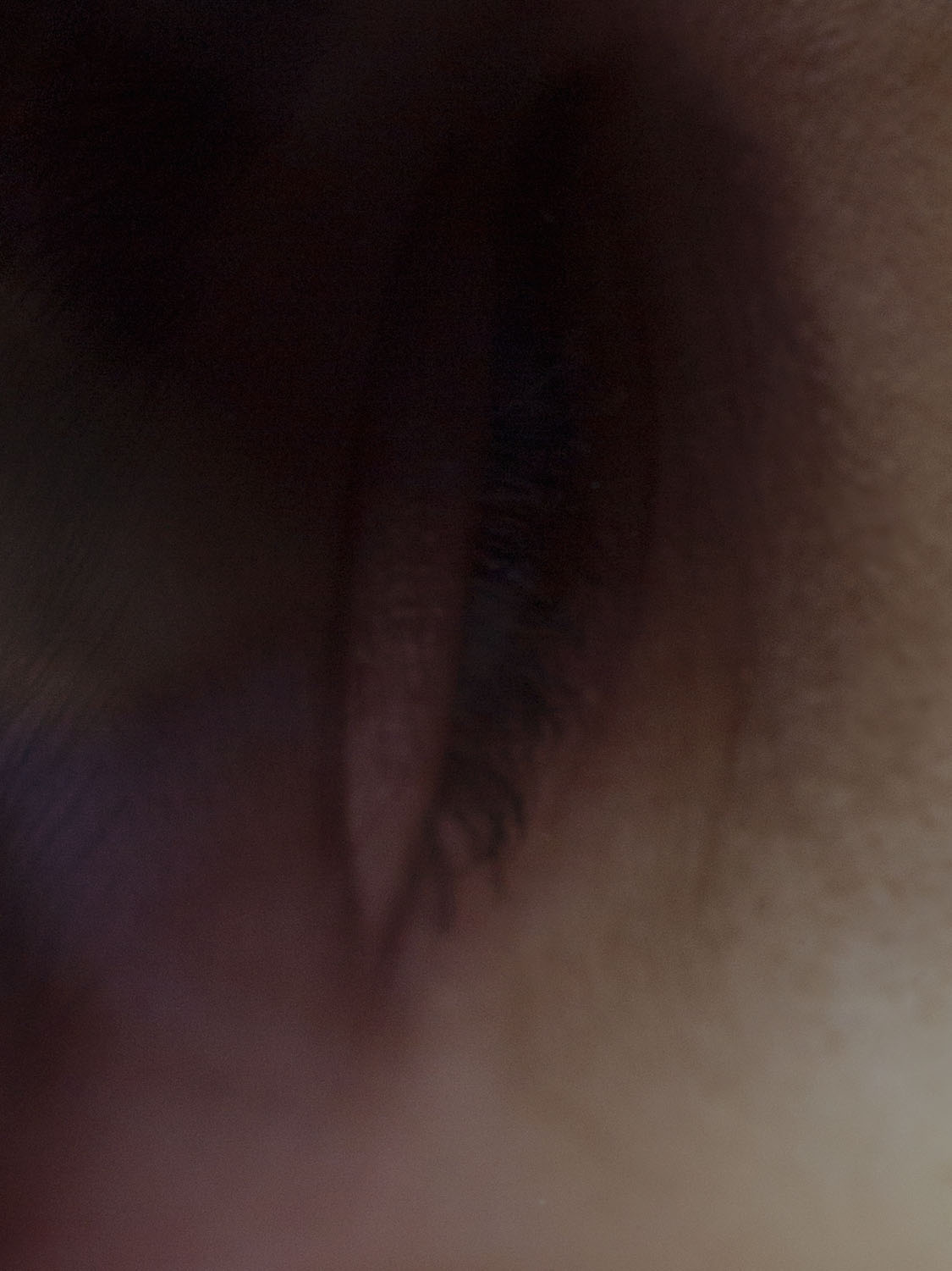 Macro shot of an eye featuring dark eyelashes and skin texture. The eye is slightly open with a shallow depth of field.