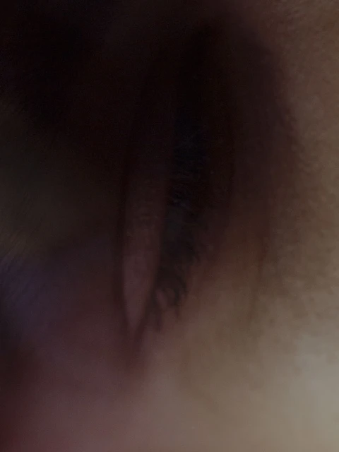 Macro shot of an eye featuring dark eyelashes and skin texture. The eye is slightly open with a shallow depth of field.