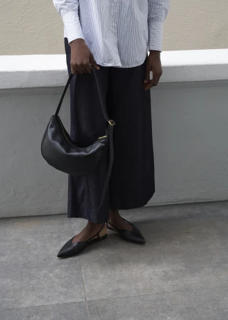 Fashionable outfit featuring a woman holding a black leather purse, paired with a striped shirt, dark pants, and pointed black shoes, outdoors.