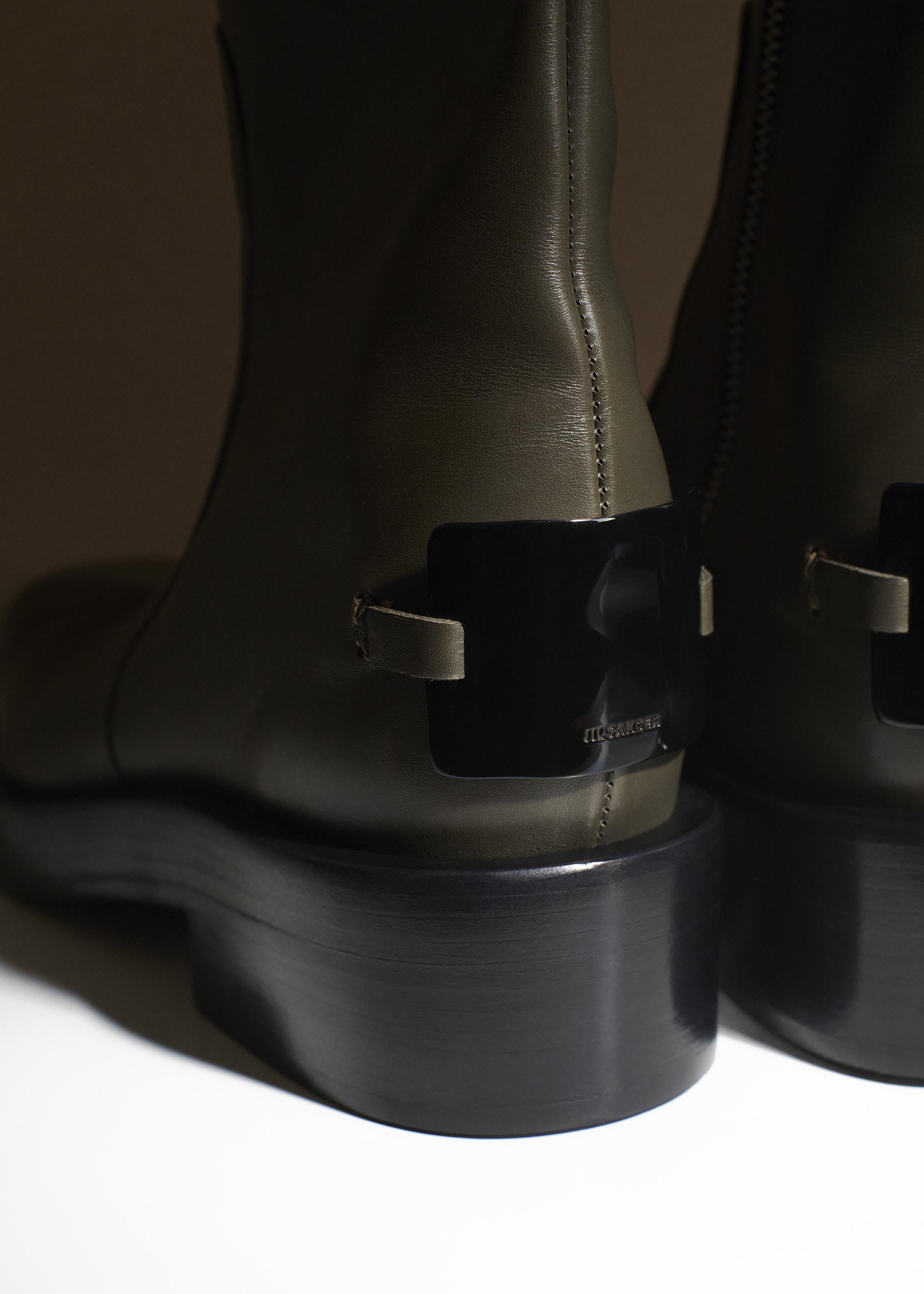 Close-up of two olive green leather ankle boots with black platform heels, against a neutral background, showcasing fashion footwear.