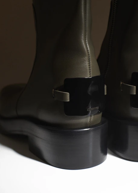 Close-up of two olive green leather ankle boots with black platform heels, against a neutral background, showcasing fashion footwear.