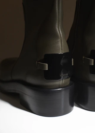 Close-up of two olive green leather ankle boots with black platform heels, against a neutral background, showcasing fashion footwear.