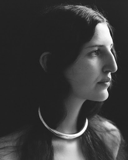 Monochrome portrait of a woman in profile wearing a metal choker necklace against a dark background in a photo studio.