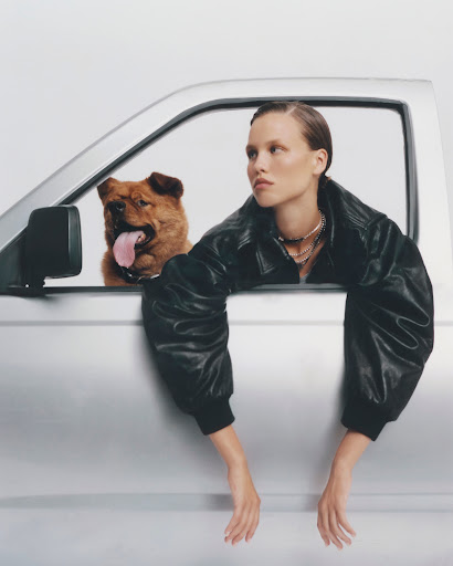 Adult woman in a black leather jacket with a Chow Chow dog in the silver truck leaning out of the window on a white background.