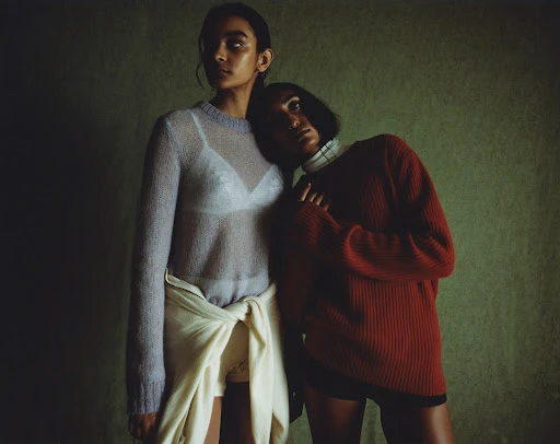 Two women posing together against a textured green background with hair styled by Kelly Peach.