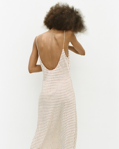 Model with afro hair seen from behind wearing a patterned slip dress against a white background