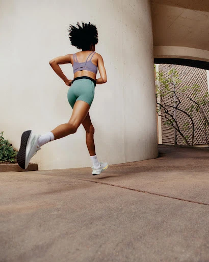 Athletic woman running outdoors, viewed from behind. She wears fitness apparel and running shoes, captured in a dynamic, low-angle shot.