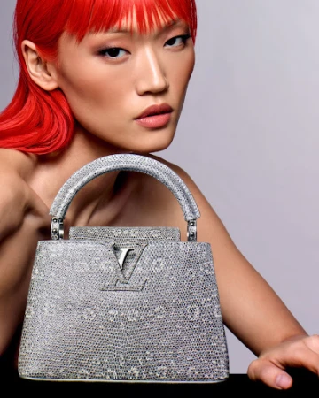 A woman with fair skin and red hair, dressed in a pale peach dress, poses in a photo studio with a pale peach background.