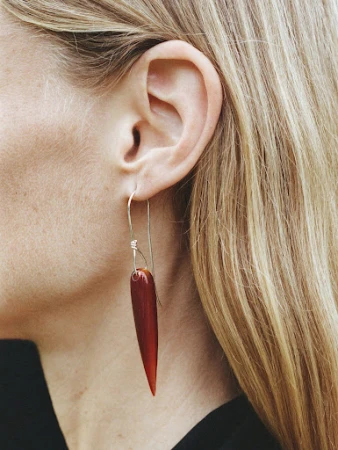 Close-up portrait of a woman wearing a long amber drop earring with blonde hair and black top