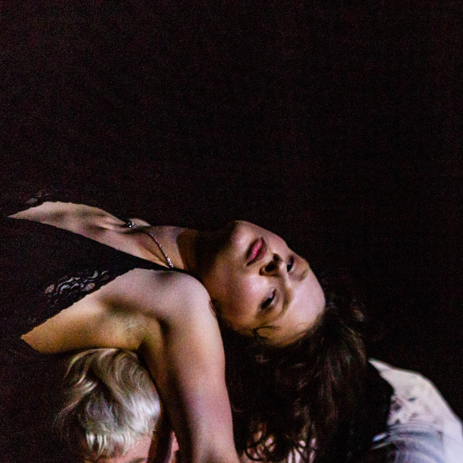 Eye-level shot of two women in dark clothing, one with dark hair and one with blonde hair, laying down against a dark background.