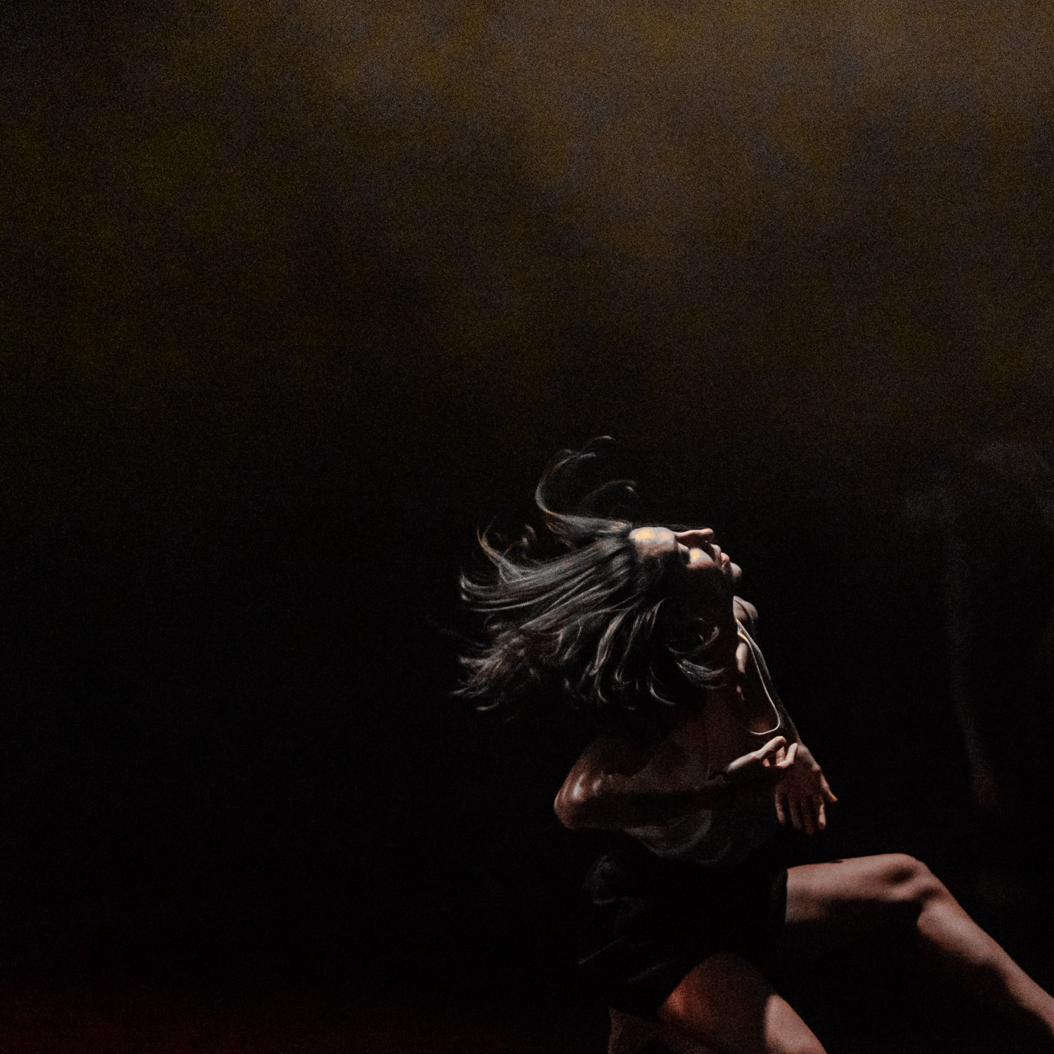 A woman with dark hair is captured mid-dance, her hair flowing as she arches back in a dimly lit space, creating a dynamic moment.