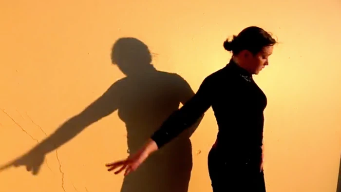 Dancer in black turtleneck performing choreography against a warm wall with shadow cast by Lisa Maris McDonell