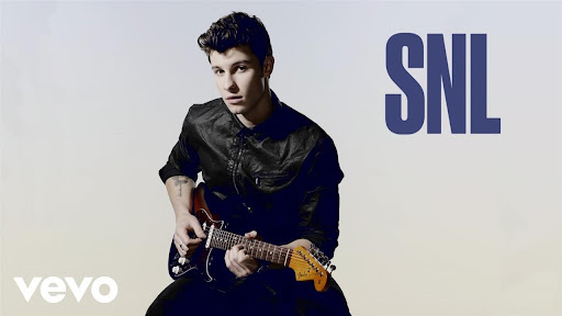 Portrait of musician Shawn Mendes playing an electric guitar against a gradient white backdrop, featuring the SNL logo.