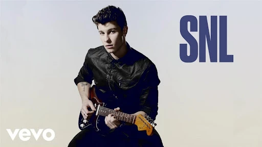 Portrait of musician Shawn Mendes playing an electric guitar against a gradient white backdrop, featuring the SNL logo.