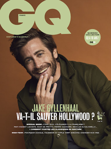 Jake Gyllenhaal smiles on the cover of GQ France magazine. He wears an olive green jacket. The background is a solid burnt orange.