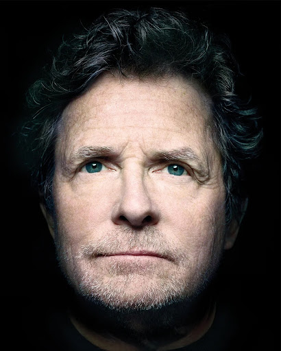 Headshot of an adult man with dark hair and blue eyes against a black background, showcasing his face and expression in detail.