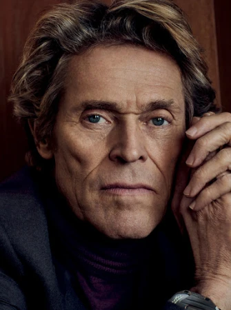 Portrait of Willem Dafoe looking serious. The actor is wearing a dark jacket and turtleneck and has a neutral expression on his face.