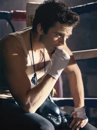 Portrait of actor Sebastian Stan with hand-wraps and boxing gloves, seated near a boxing ring